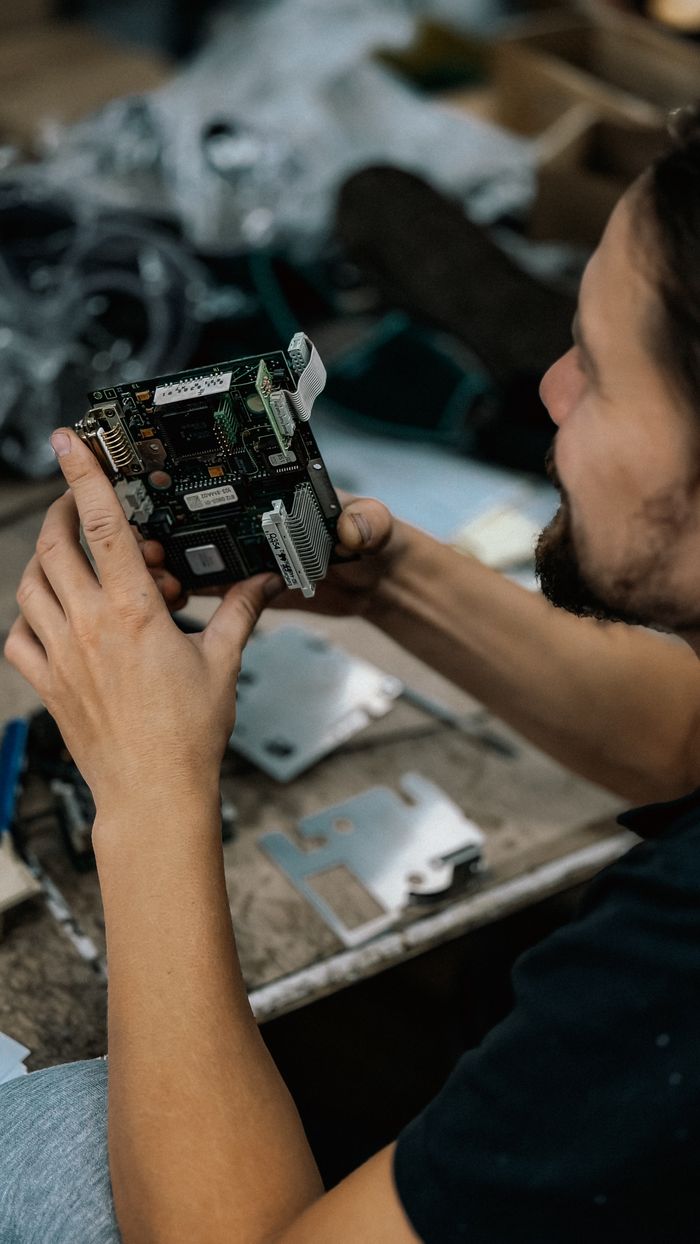 services-04 Focused technician examining a circuit board with precision in a cluttered workshop environment.